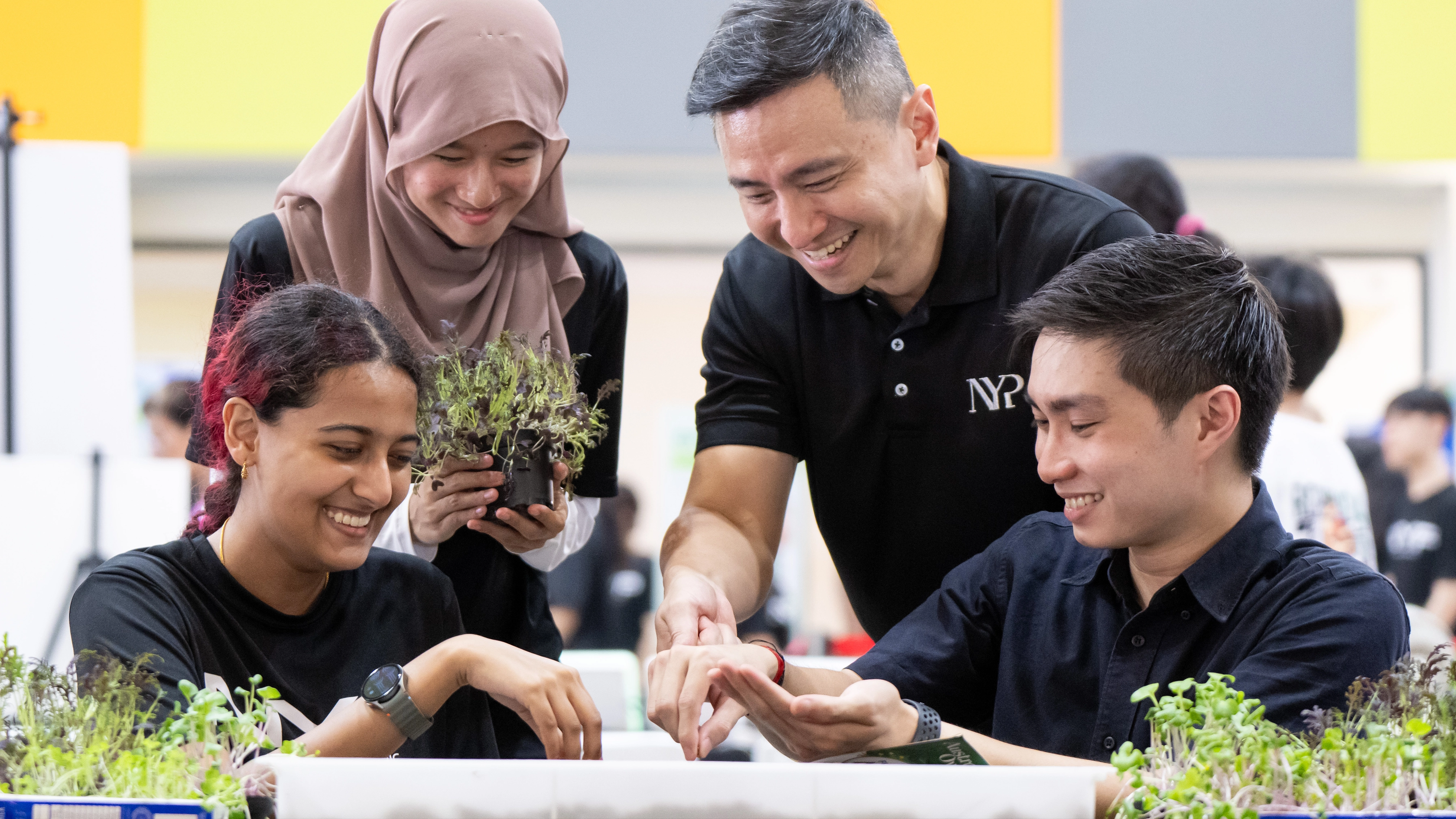 A lecturer and two students discussing about a sustainability project. The lecturer is holding a potted plant.