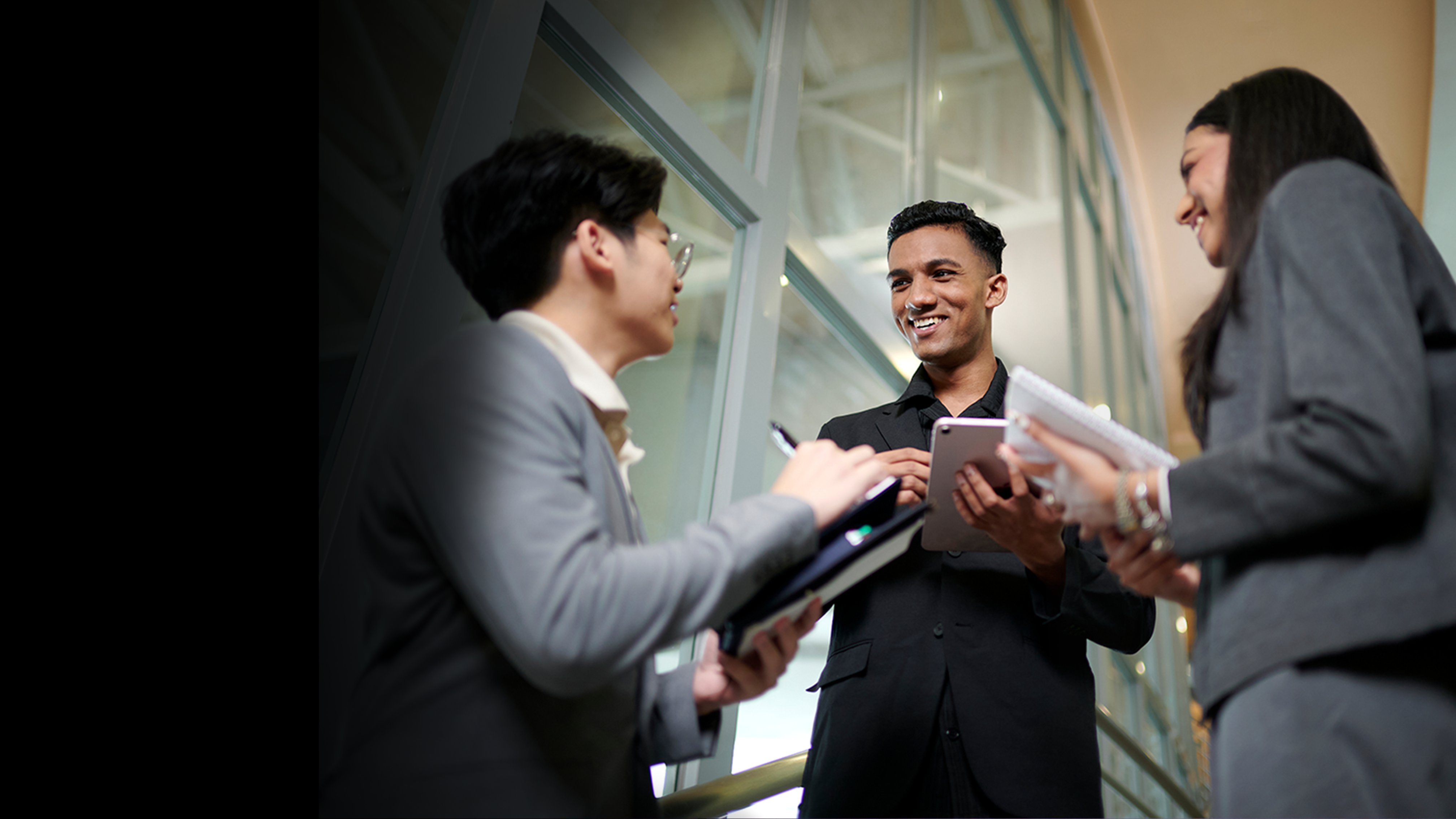 Man confidently smiling, in conversation with two counterparts in officewear.