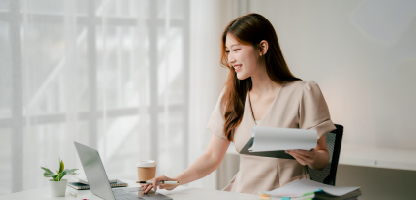 Woman wearing white dress looking at laptop in white room