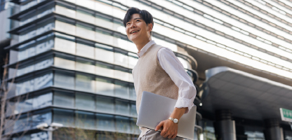 Man with white sleeves carrying laptop in front of a building