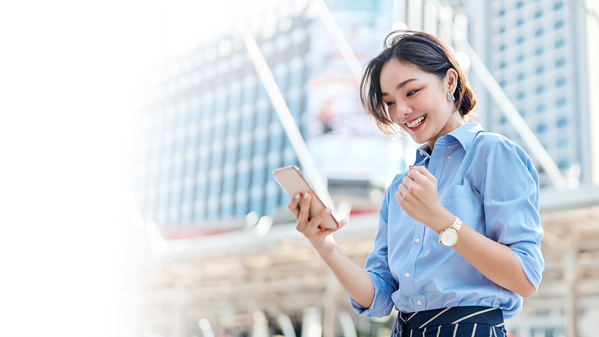 Woman in smart-formal attire looking at her phone with a big smile