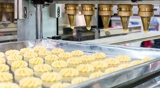 close up dough or cream and nozzle discharge of automatic biscuit or sweets making machine in production line for high technology of industrial food manufacturing