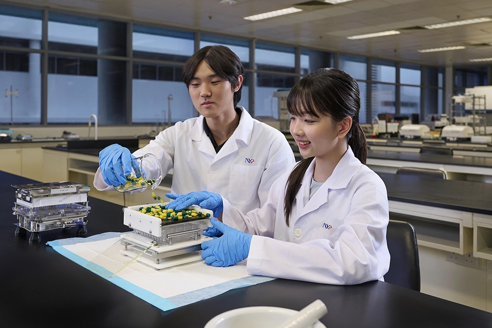 Two students in lab coats using pharmaceutical equipments to make pills.