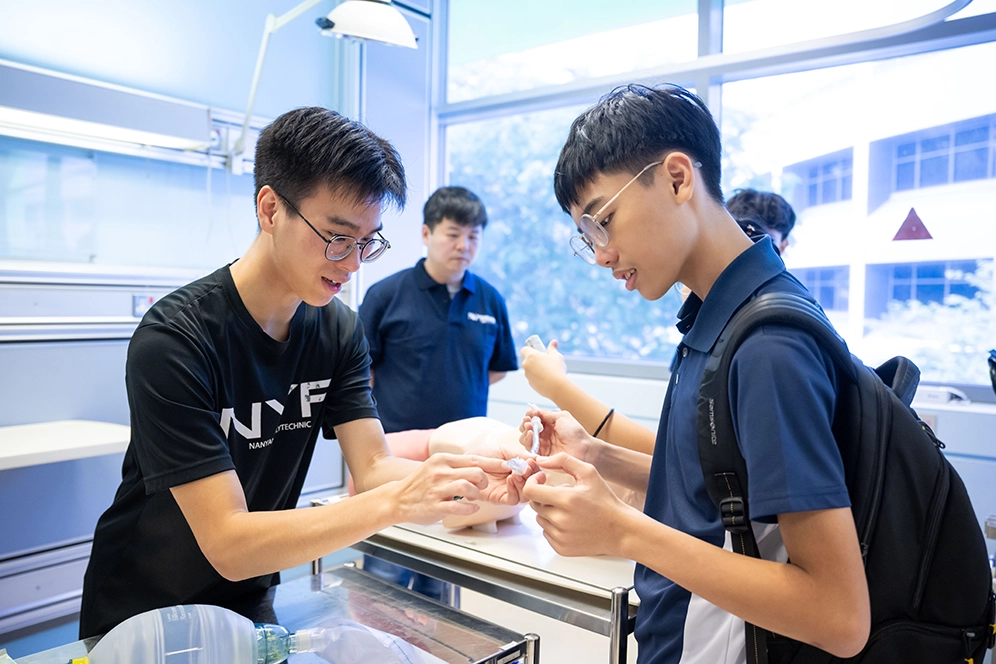 A boy is guided by a NYP student to use a medical equipment.