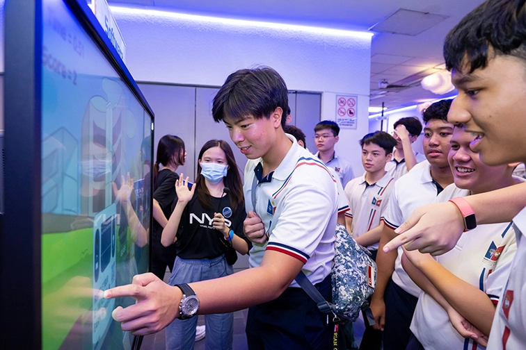 A boy interacting with a touchscreen as his friends and the NYP student guide looks on.