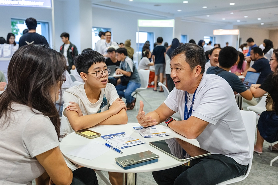 A NYP lecturer speaking to a boy and his parent at a table.