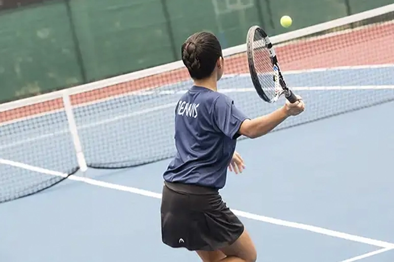 Back view of a female tennis player hitting a tennis ball